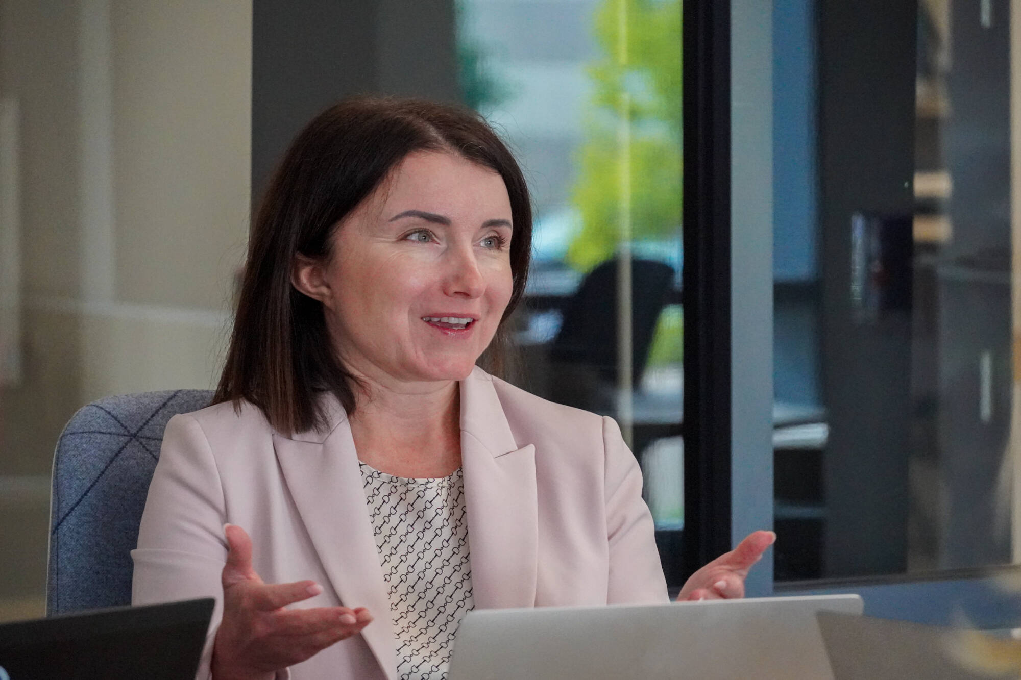 Yuhila Chiaburu, co-founder of The Mitten Project, speaks and gestures during a collaborative discussion, seated at a conference table with a laptop open in front of her.
